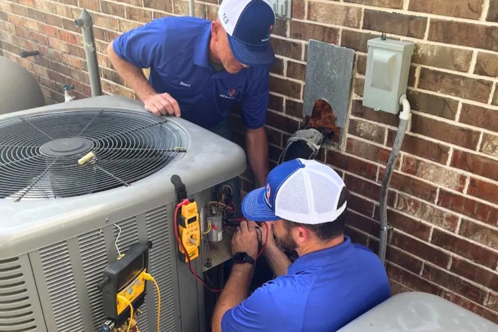 Reed and Ryan Loewe repairing HVAC unit outside of brick home