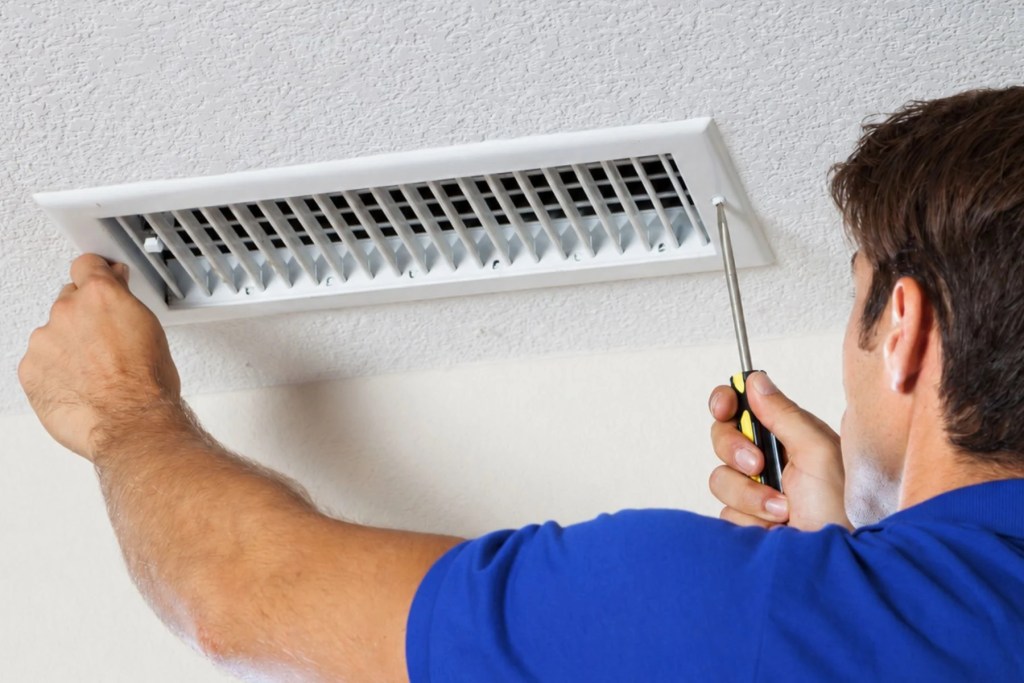 HVAC team member unscrewing air vent in ceiling for duct cleaning